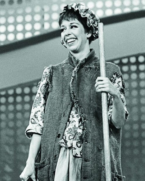 A black and white photograph of Carol Burnett in a costume and holding a wooden stick.
