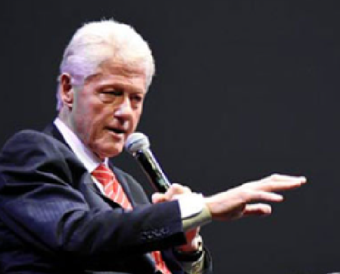 Bill Clinton wearing a suit and tie delivering a speech with a microphone in his hand.