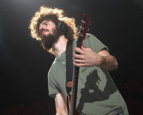 Brad Delson in a green shirt playing guitar in a dark studio setting.