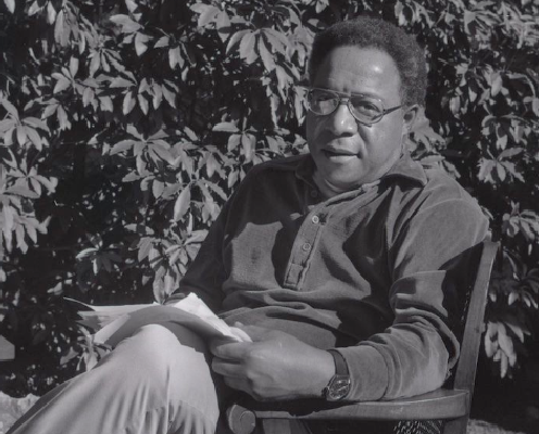 A black and white photograph of Alex Haley sitting outside with leaves in the background.