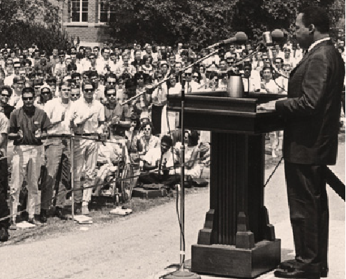 A black and white photograph of Martin Luther King Jr. standing at a podium in front of an audience.