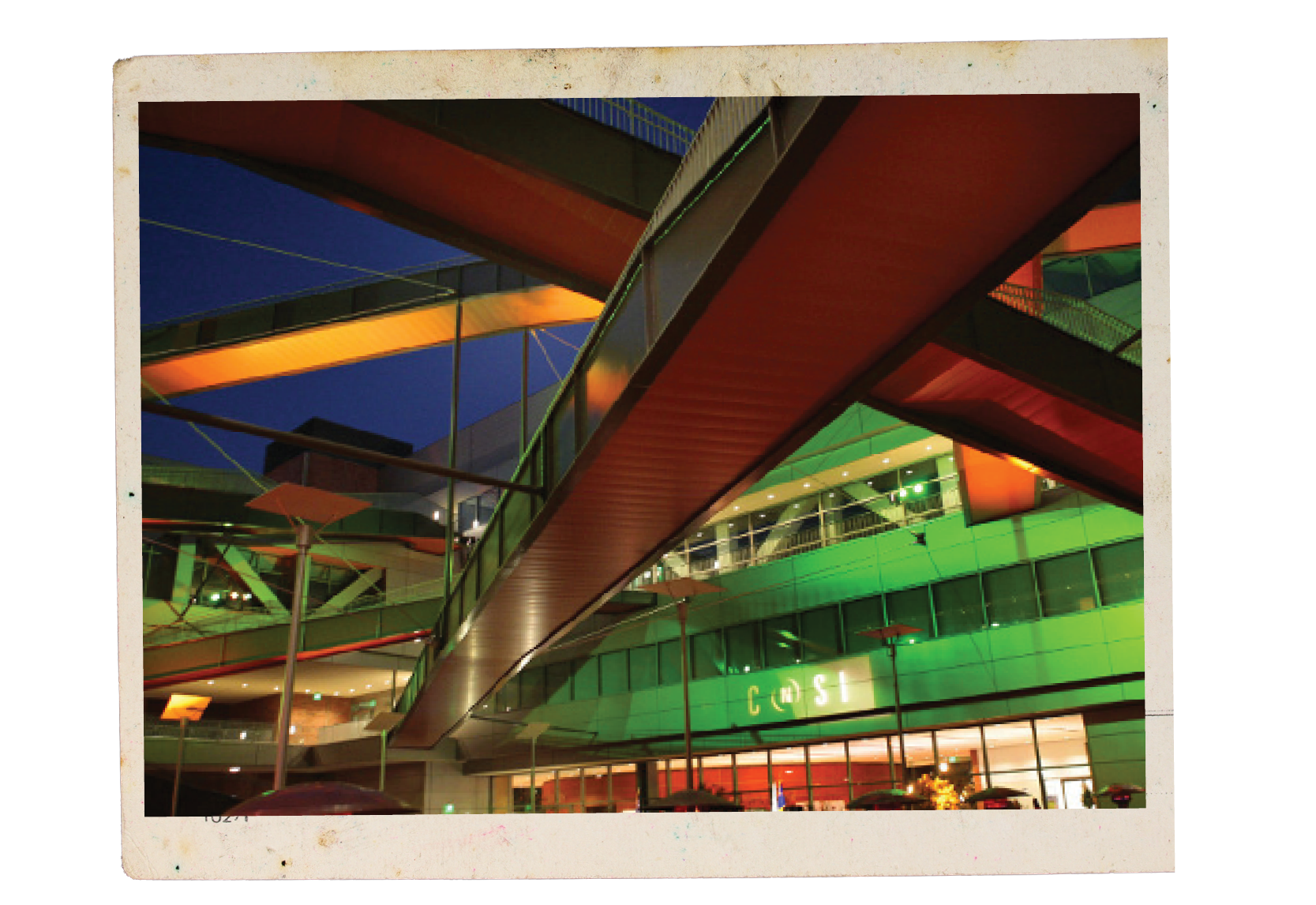 The California NanoSystems Institute illuminated by green and orange lights, a dark-blue night sky in the background.