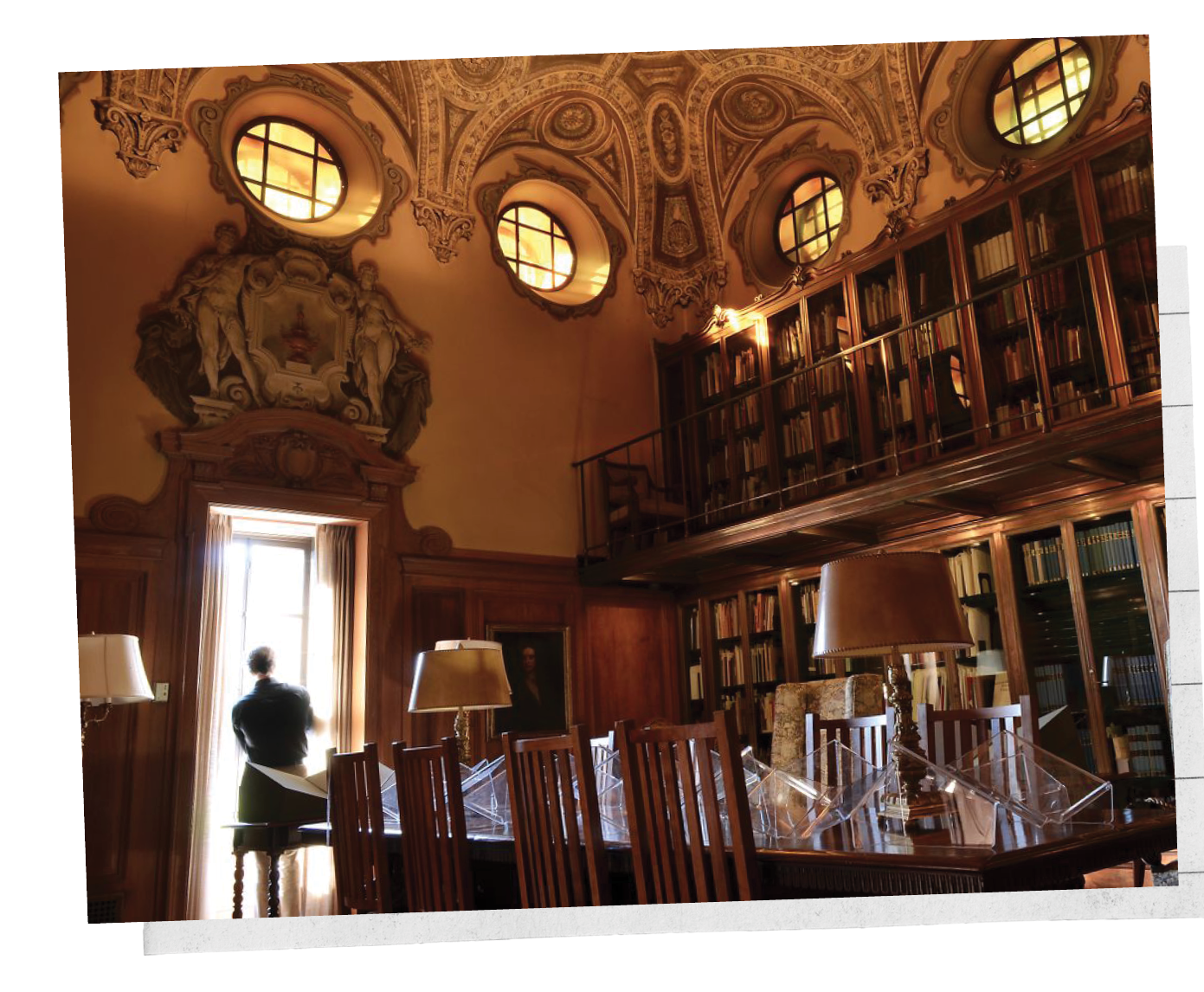 An ornate library with bookshelves, four circular windows and marble statues decorating the top of a doorway.