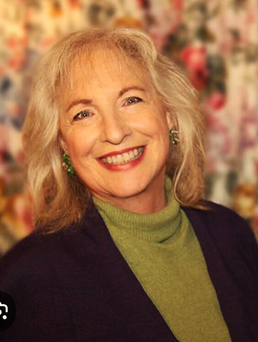 8.2020 Jacqueline Braitman in a black sport coat and green turtleneck sweater against a blurred background.