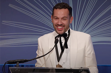 Justin Torres at a podium in a white jacket giving speech at National Book Awards ceremony