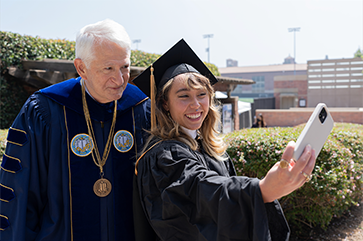 Gene Block and Katelyn Ohashi dressed in graduation regalia as they pose for a selfie.