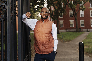 Eddie Cole in white shirt and orange vest leaning against gate.