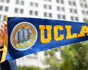 Hands holding up UCLA banner in front of Trust building.