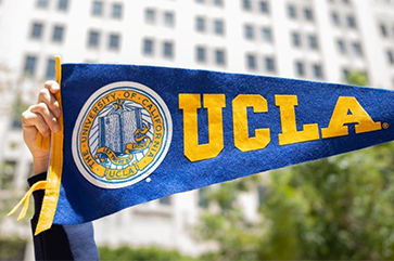 Hands holding up UCLA banner in front of Trust building.