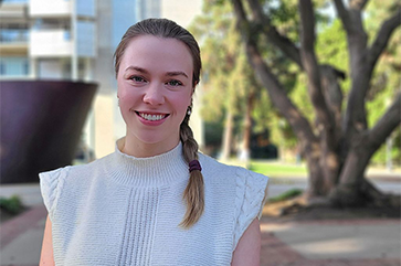 Portrait of Ekaterina (Katya) Khlystova in a white blouse standing outside on a sunny day.