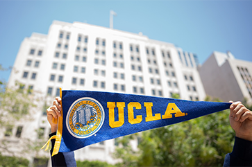 Hands holding up UCLA banner in front of Trust building