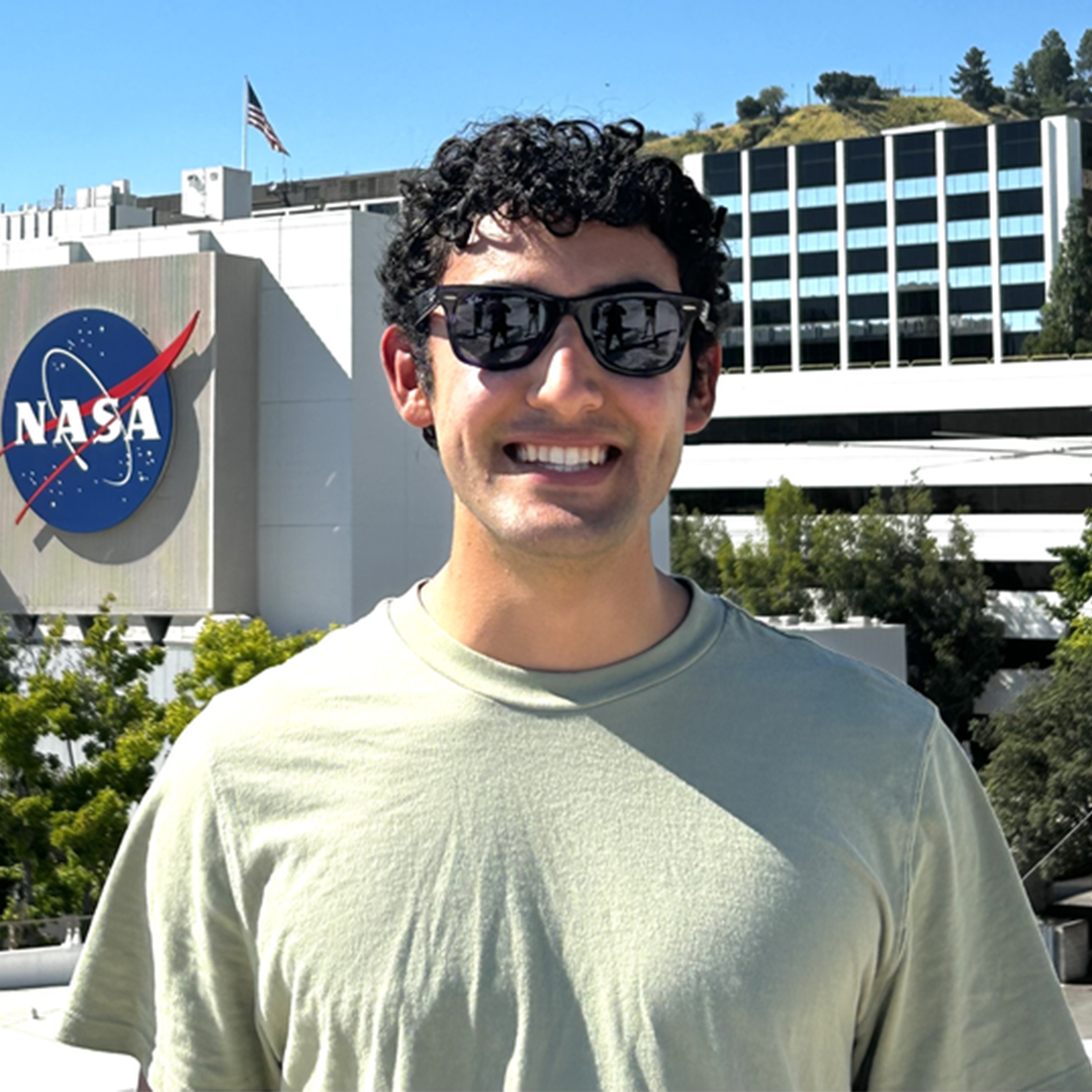 A photograph of Cheyanne Shariat wearing a light green shirt and sunglasses on a sunny day with the "NASA" logo visible in the background. 