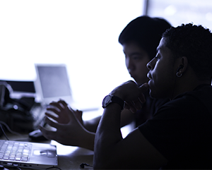 Two students silhouetted in front of a computer screen