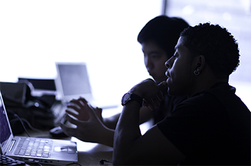Two students silhouetted in front of a computer screen