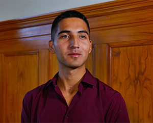 A portrait of Diego Sarmiento in a maroon dress shirt with a stained wood wall in the background.