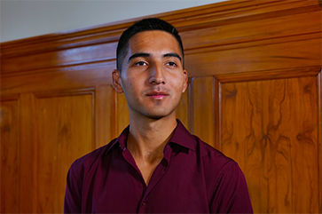 A portrait of Diego Sarmiento in a maroon dress shirt with a stained wood wall in the background.