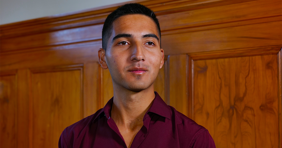 A portrait of Diego Sarmiento in a maroon dress shirt with a stained wood wall in the background.