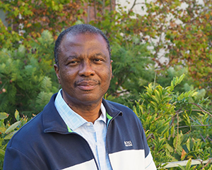 Wilfrid Gangbo in a blue and white jacket with green leaves in the background.