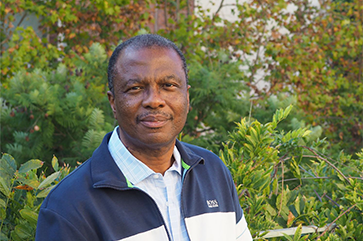 Wilfrid Gangbo in a blue and white jacket with green leaves in the background.