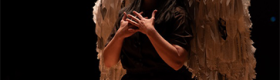 A student in the program performs at UCLA’s Glorya Kaufman Theater wearing a brown jumpsuit and white wings with tattered feathers