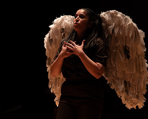 A student in the program performs at UCLA’s Glorya Kaufman Theater wearing a brown jumpsuit and white wings with tattered feathers