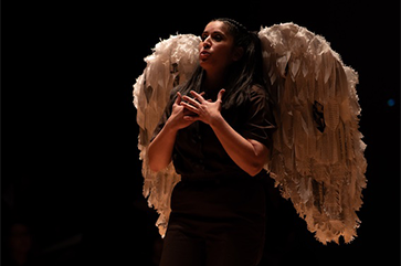 A student in the program performs at UCLA’s Glorya Kaufman Theater wearing a brown jumpsuit and white wings with tattered feathers