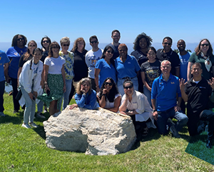 The UCLA Alumni 2023 Board of Directors standing on grass with the ocean in the background.