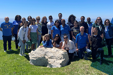 The UCLA Alumni 2023 Board of Directors standing on grass with the ocean in the background.