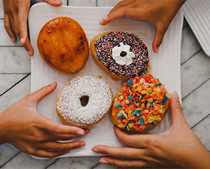 Four hands reaching for designer doughnuts