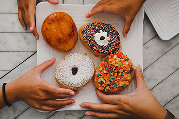 Four hands reaching for designer doughnuts