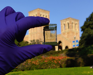 Gloved hand holding up small device with Royce Hall in the background