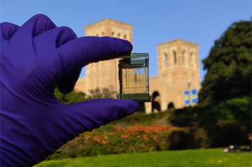 Gloved hand holding up small device with Royce Hall in the background