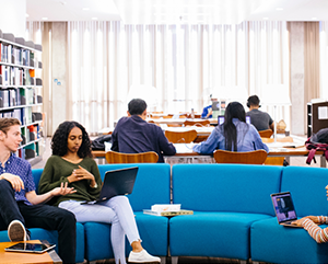 Students-inYRL-RR-363-241 Student sitting inside a well lit room with a blue couch and communal desks in the background.