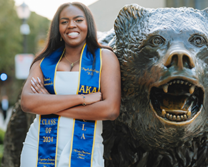 naomi+1-363-241.jpg Naomi Hammonds wearing graduation sash, stands next to bear statue