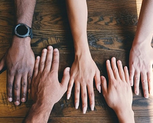 Hands-different-skin-tones-363-241 Five hands with different skin tones on a wooden table view from above.