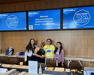 McNair-conference-363-241 Four people stand below screen with 2023 UCLA National McNair Conference