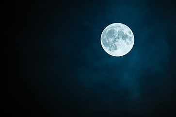 A full moon against a black night sky with some faint clouds.