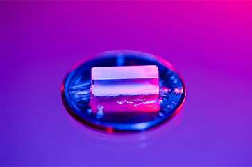 A close-up photograph of a thorium-229 atom with a blue and purple light illuminating the background.