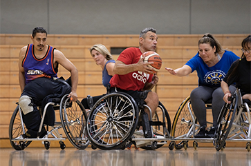 An action shot of five players who participate in UCLA Open Rec wheelchair basketball, with Alvin Malave holding the ball.