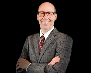 Jack Bobo Official Photo – 363 – 241 Jack Bobo in a grey suit and red tie against a black background.