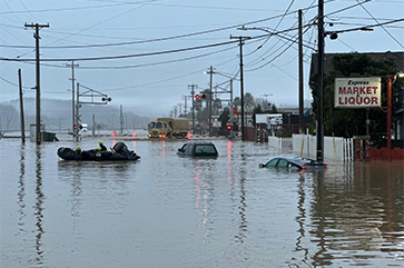 Submerged cars float in the forefront as a National Guard vehicle approaches a flooded railroad track in Monterey County California