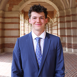 Lev Afonine in a blue suit and tie, posing in the corridor of Royce Hall. 