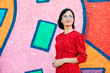Carribean Fragoza wearing red dress standing in front of brightly colored wall.
