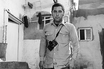 A black and white photograph of Jason De León wearing a camera.