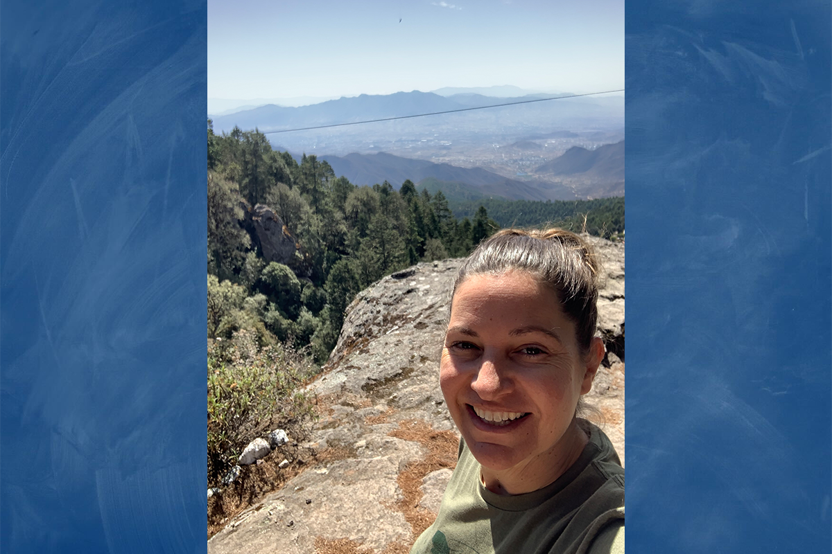 Julie Bernard standing on a mountain lookout point with a mountainous valley in the background.