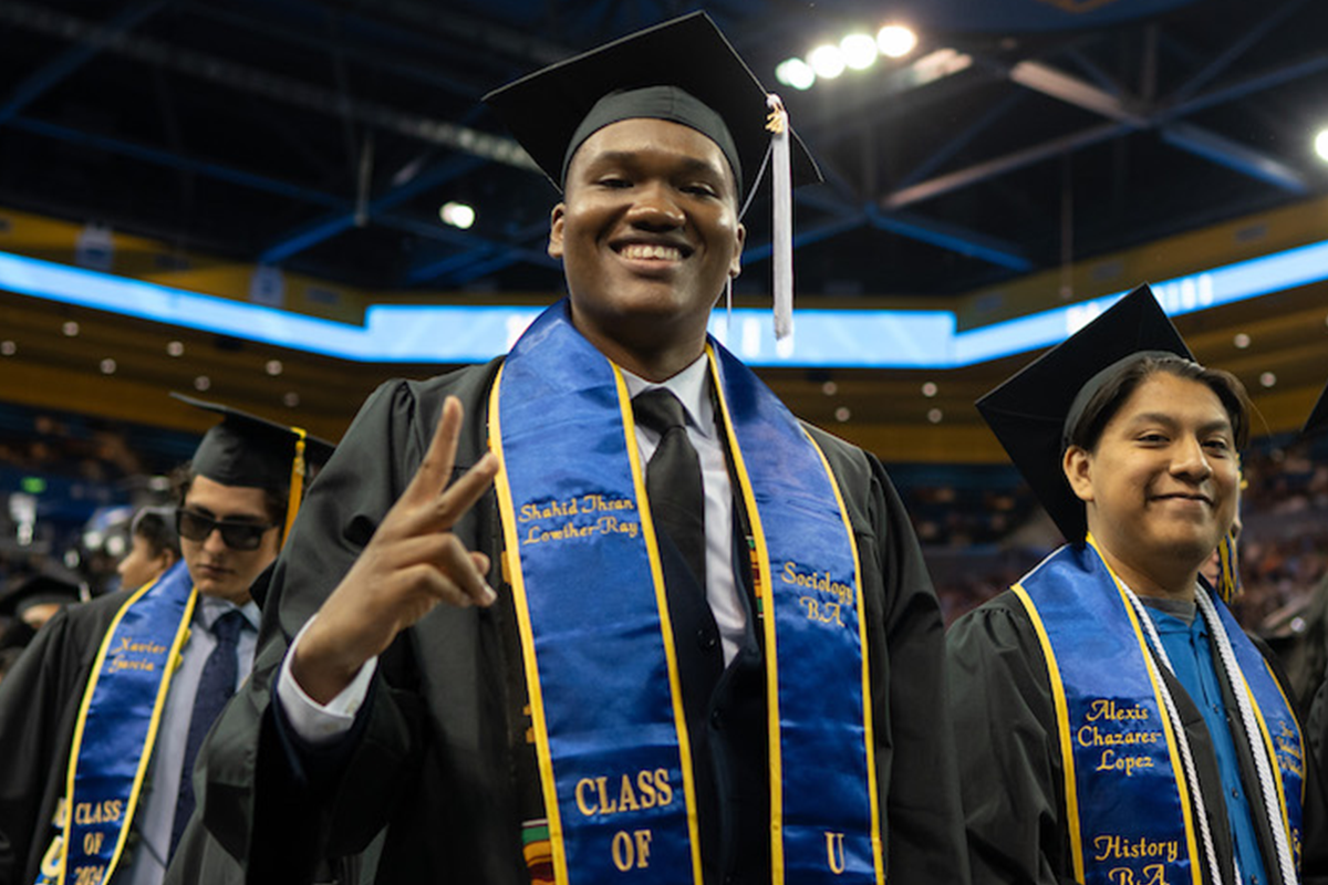 Student throws up peace sign while standing with fellow graduates in Pauley Pavilion