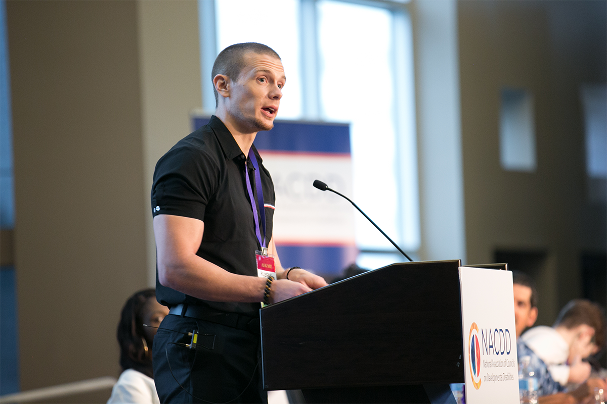 Russell Lehmann in a black polo standing and speaking from a podium.
