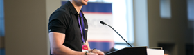 Russell Lehmann in a black polo standing and speaking from a podium.