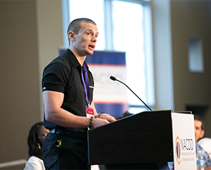 Speaking+RL-363-241 Russell Lehmann in a black polo standing and speaking from a podium.