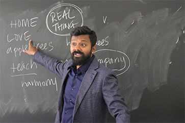 Vetri Nathan pointing at words on a chalkboard while teaching global food studies class
